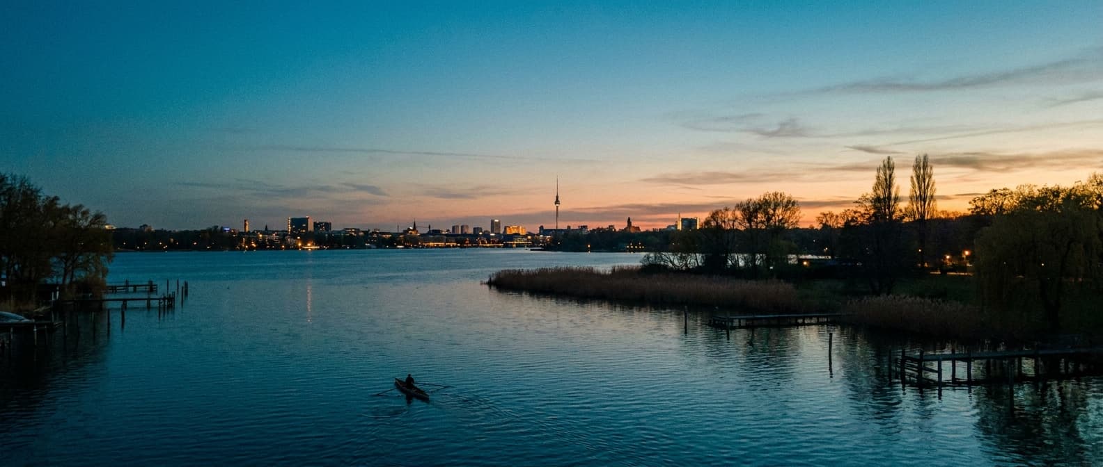 Berliner Skyline-Silhouette spiegelt sich auf ruhigem Wasser, kleines Ruderboot